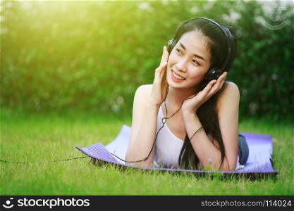 young woman listening to music with headphones and laying on a grass field