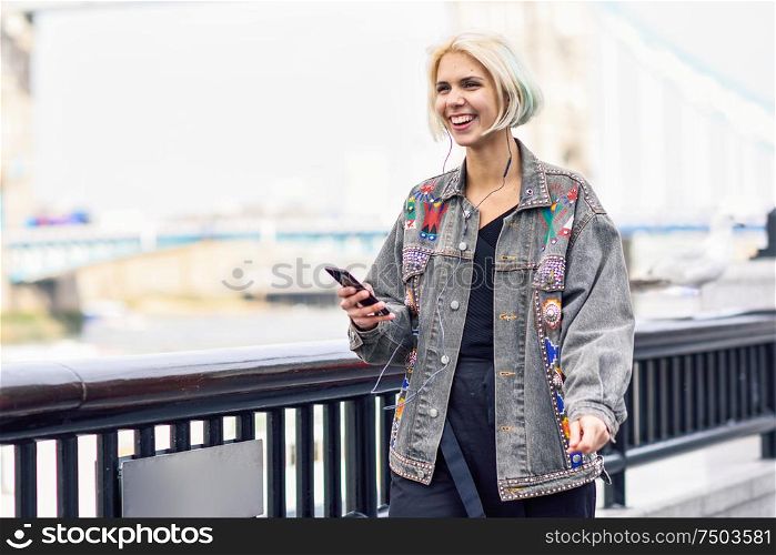 Young woman listening to the music with earphones and smart phon in urban background. Thames River in London.. Young woman listening to the music in urban background.