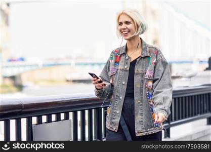 Young woman listening to the music with earphones and smart phon in urban background. Thames River in London.. Young woman listening to the music in urban background.