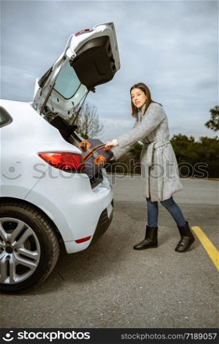 Young woman loading her luggage into the car trunk