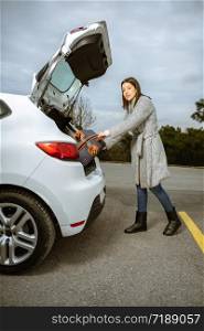 Young woman loading her luggage into the car trunk