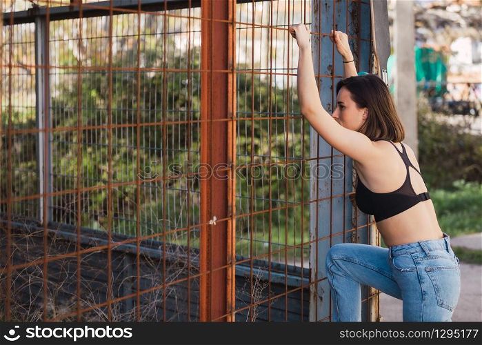 Young woman look inside through a fence in a ancient industrial street