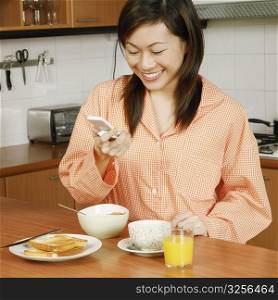 Young woman looking at a mobile phone and smiling at a kitchen counter