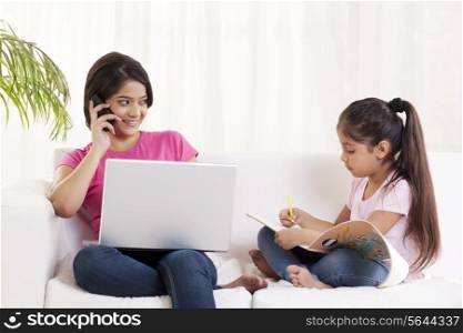 Young woman looking at daughter while talking on cell phone