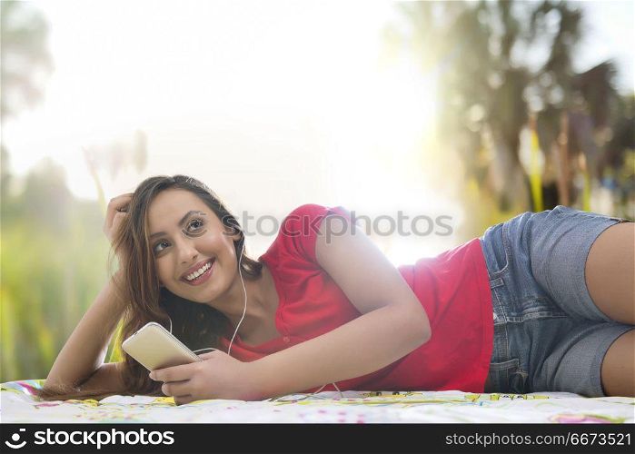 Young woman looking at her cell phone in a park and listening music