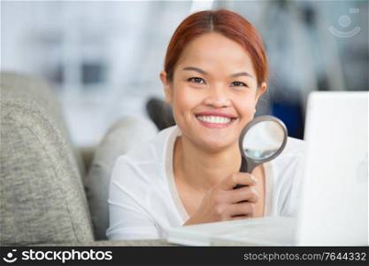 young woman looking at her laptop with a magnifying glass