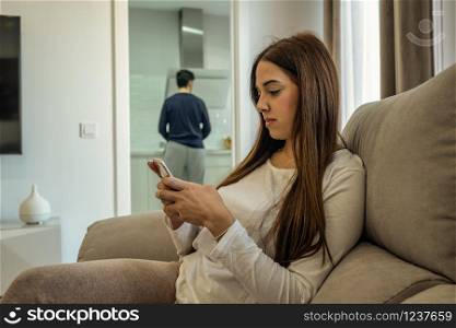 young woman looking at her mobile while her husband does the housework. concept of gender equality