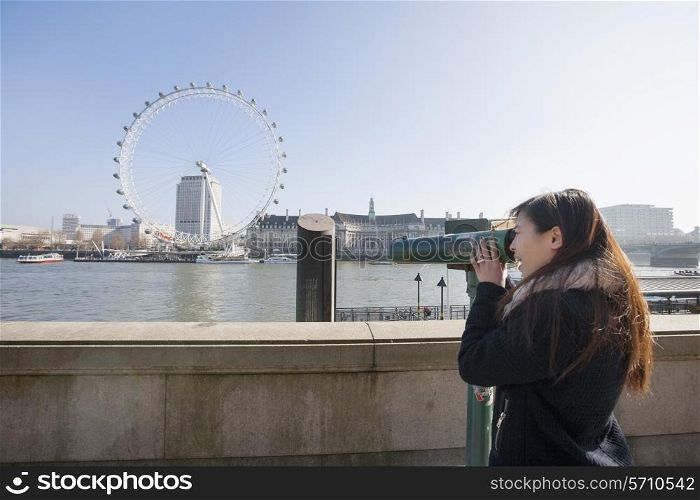 Young woman looking at London Eye through stationary viewer at London; England; UK