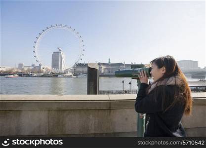 Young woman looking at London Eye through stationary viewer at London; England; UK