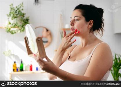 Young woman looking at the mirrow and examine her face in white bathroom. Wellness and body positivity. Young woman looking looking at the mirrow