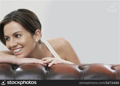 Young woman looking away while leaning on sofa against gray background