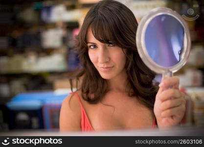 Young woman looking in handheld mirror in beauty store