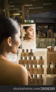 Young woman looking in mirror and sampling cosmetics at beauty supply store