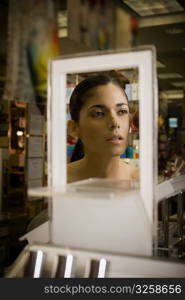 Young woman looking in mirror and sampling cosmetics at beauty supply store