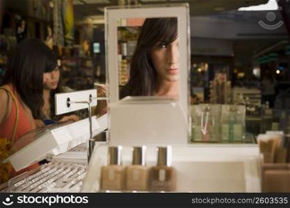 Young woman looking in mirror and sampling cosmetics in beauty supply store