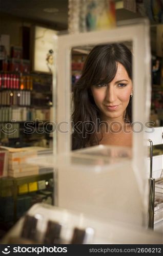 Young woman looking in mirror and sampling cosmetics in beauty supply store