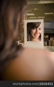 Young woman looking in mirror and sampling cosmetics in beauty supply store