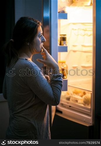 Young woman looking in the refrigerator at late evening