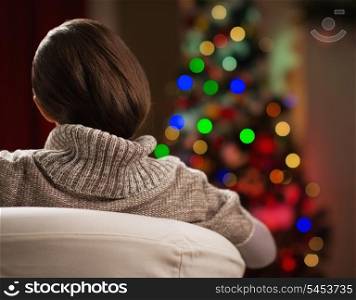 Young woman looking on Christmas tree. Rear view
