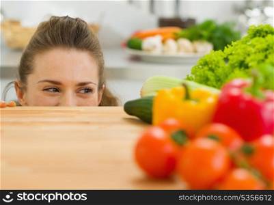 Young woman looking out from cutting board and looking on vegetables