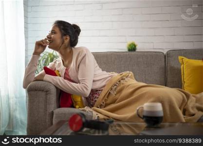 Young woman looking out of window while lying on sofa in living room