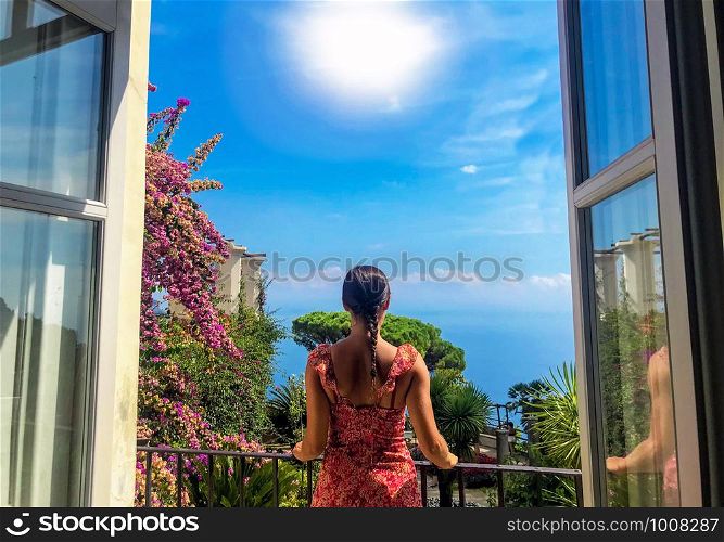 Young woman looking out the window of her balcony at wiew of famous Amalfi Coast with Gulf of Salerno from Villa Rufolo gardens in Ravello, Campania, Italy, 2019. Travel destinations in Europe, Italy