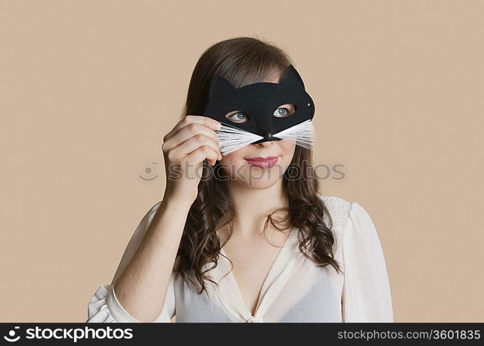 Young woman looking through eye mask over colored background