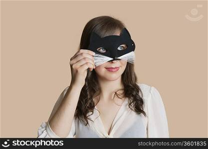 Young woman looking through eye mask over colored background