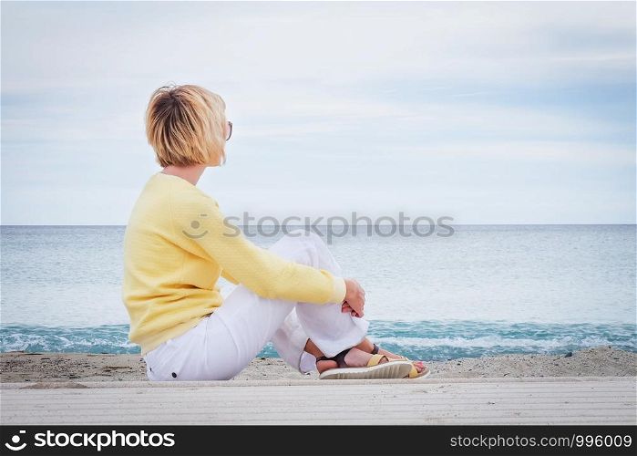 Young woman looking through the sea while sitting on beach outdoors. Woman looking through the sea while sitting on beach