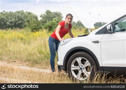 Young woman looking under the hood of overheated car