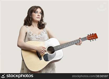 Young woman looking up while playing guitar against gray background