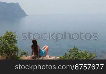 young woman looks at the sea while sitting on the edge of a cliff black sea, Balaklava, Crimea, Ukraine