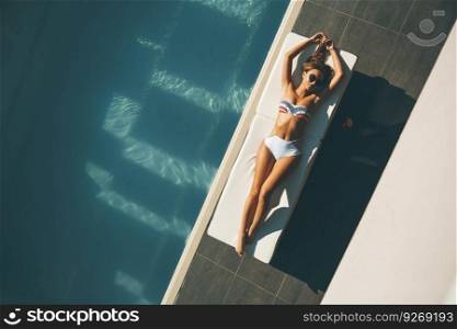 Young woman lying by swimming pool  at hot∑mer day