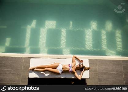 Young woman lying by the pool on sunbed at ot summer day