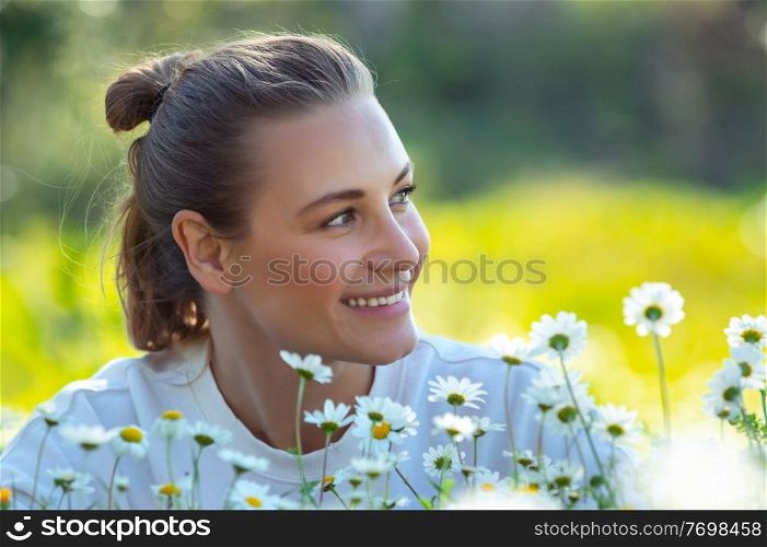 Young woman lying down on the fresh green grass among little gentle daisy flowers and smiling, enjoying beauty and freshness of spring nature