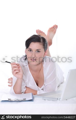 Young woman lying down with a laptop computer and clipboard