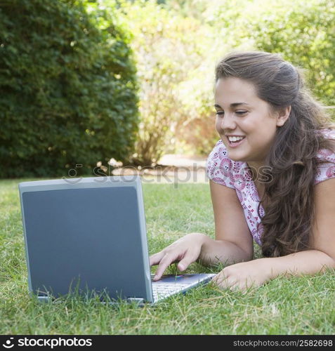 Young woman lying in a park and using a laptop