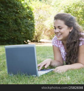 Young woman lying in a park and using a laptop