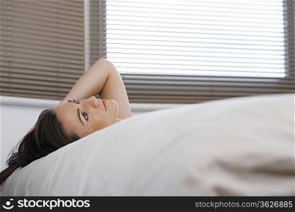 Young woman lying in bed, looking up