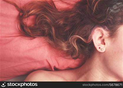 Young woman lying in bed with her hair strewn across the pillow
