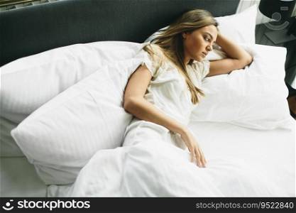 Young woman lying in bed with white linen