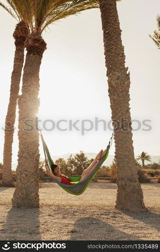 Young woman lying in his hammock among palm trees on the beach