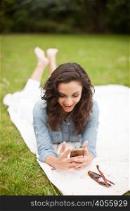 Young woman lying in park looking at mobile phone, smiling
