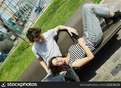Young woman lying on a bench resting her head in the lap of a young man