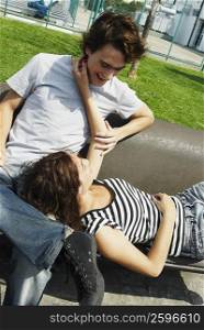 Young woman lying on a bench resting her head in the lap of a young man