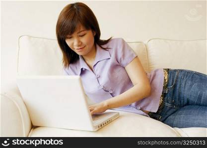 Young woman lying on a couch and working on a laptop