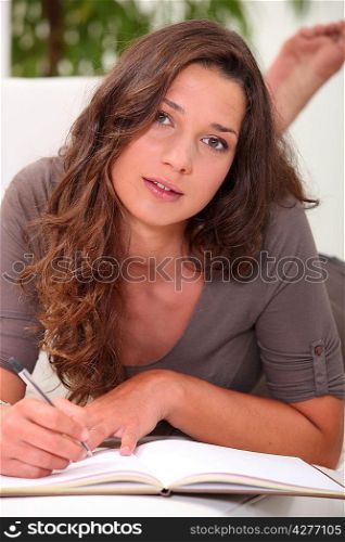 Young woman lying on a couch writing in a book