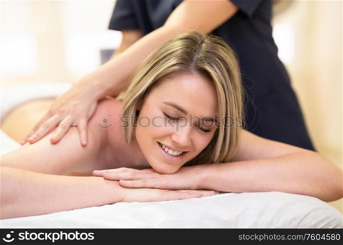 Young woman lying on a stretcher receiving a back massage in a physiotherapy center.. Woman lying on a stretcher receiving a back massage.