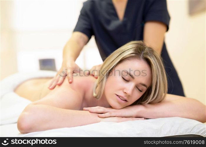 Young woman lying on a stretcher receiving a back massage in a physiotherapy center.. Woman lying on a stretcher receiving a back massage.