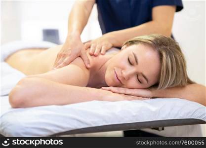 Young woman lying on a stretcher receiving a back massage in a spa center.. Woman lying on a stretcher receiving a back massage.